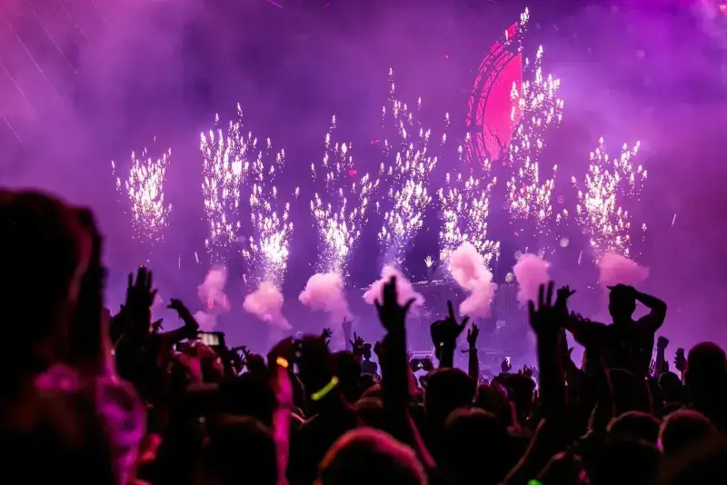 Crowd dancing under purple lights and pyrotechnics at a rave festival